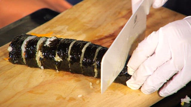 Cutting gimbap with a knife on a wooden cutting board