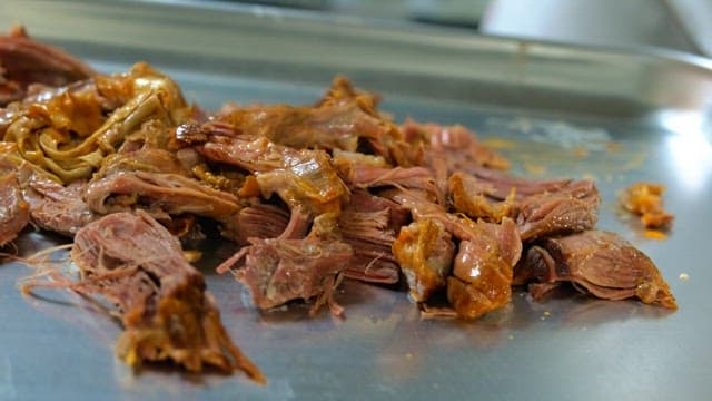 Preparing boiled meat on a metal tray with gloved hands