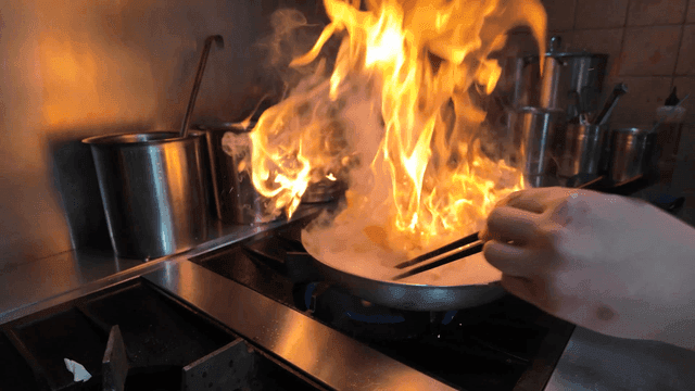 Chef stir-frying in flame-lit pan in kitchen