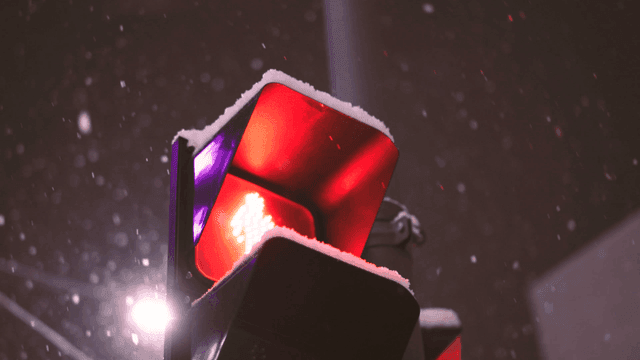 Snow falling on a red traffic light at night