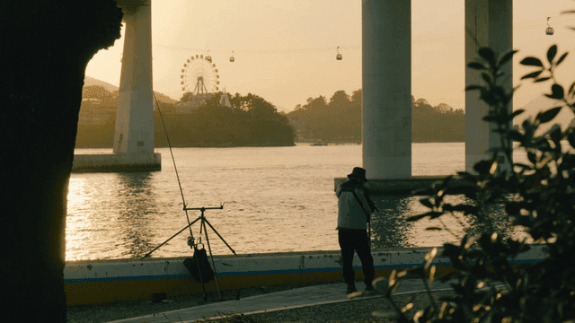 Back of man fishing on riverbank at sunset