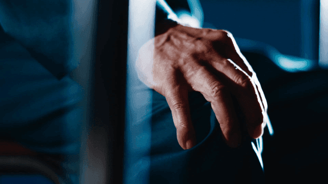 Old man with his hands on his knees in dark room