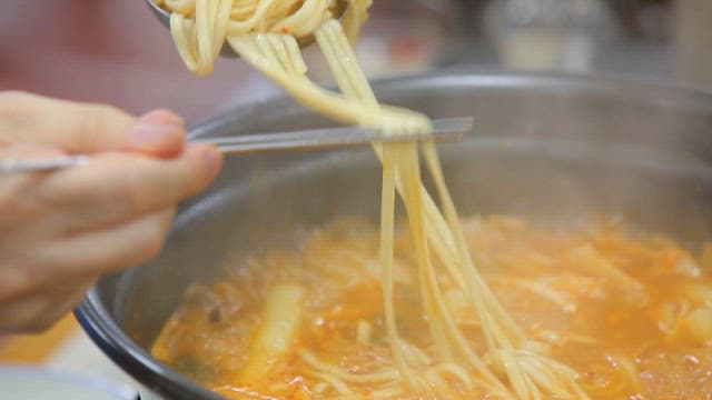 냄비에서 끓고 있는 매운 닭칼국수에서 집어 든 국수