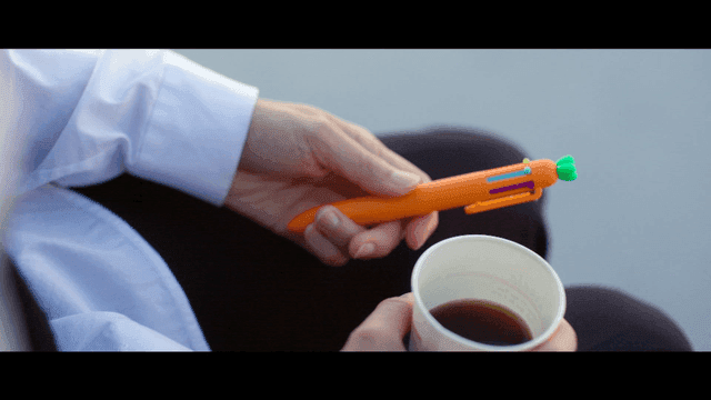 Person holding carrot-shaped pen and coffee