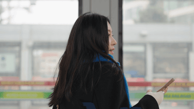 Profile of a woman waiting at a train station looking at her cell phone