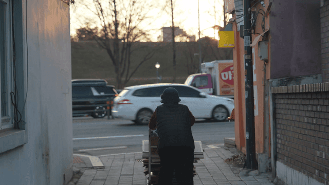 Back of old man pushing cart of waste paper on street