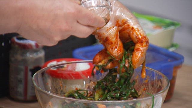 Mixing sesame oil with green onion kimchi in a glass bowl