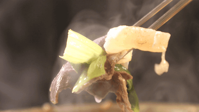 Chopsticks picking up Hanwoo hot pot containing meat and vegetables