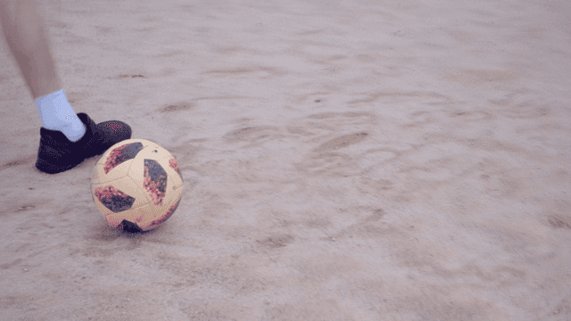 모래 운동장 위의 축구공에 슈팅을 차는 사람