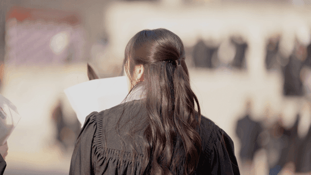 Back view of graduates holding bouquets at graduation ceremony