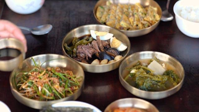 Hand Putting Soy Sauce on a Table with Various Side Dishes