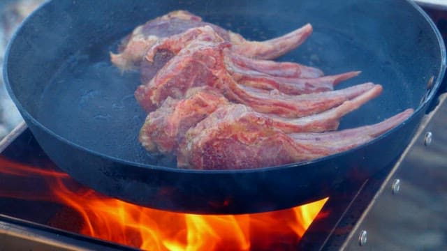 Fresh lamb being cooked in a frying pan on the portable stove