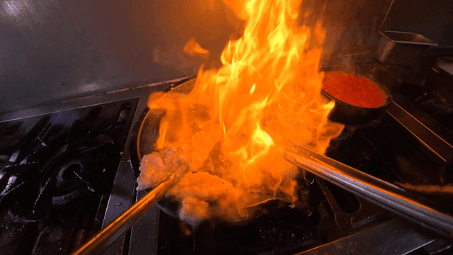Grilled large intestine cooked in pan over blazing flame in kitchen
