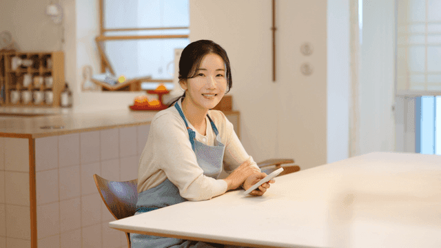 Woman wearing apron holding smartphone at table