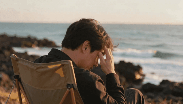 Man sitting by sea at sunset with his head covered