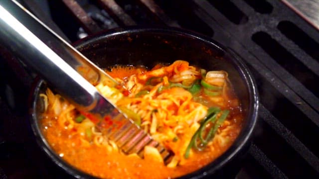 Stirring boiling ramyeon with tongs