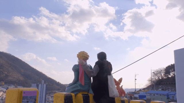 언덕 마을을 내려다보는 조각상과 사진 찍는 여성