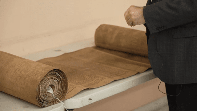 테이블 위 고대 두루마리를 설명하는 사람