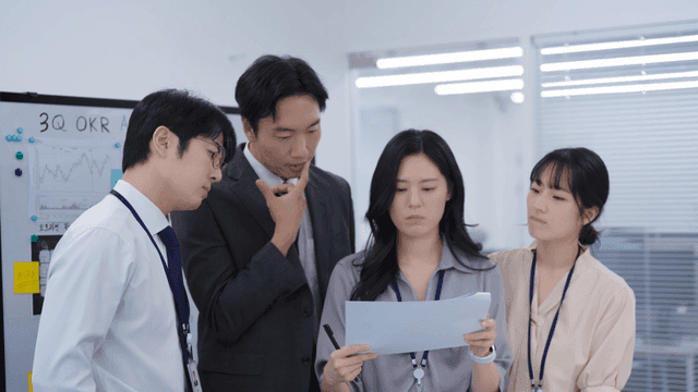 다같이 서서 진지하게 회의 문서를 체크하는 팀원들