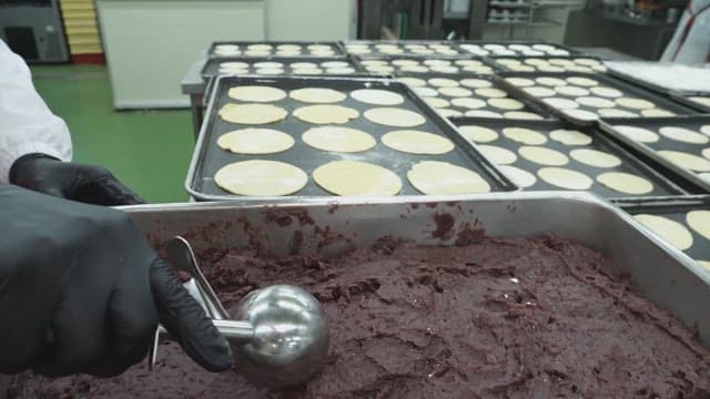 Worker filling red bean paste onto dough on a tray in a bakery kitchen