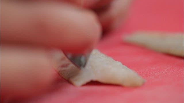 Removing bones from fish fillets on a red cutting board