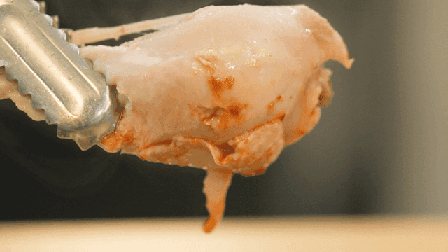 Whole chicken held with tongs, chicken leg