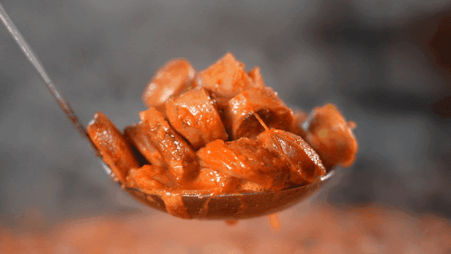 Ladle scooping sausage from hot budaejjigae