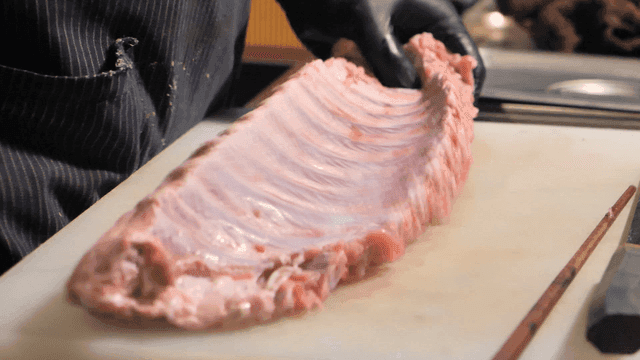 Chef removing rib fascia on cutting board