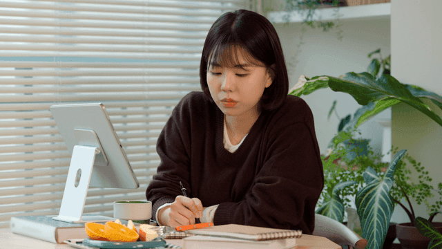 Young woman studying at her desk looking at tablet