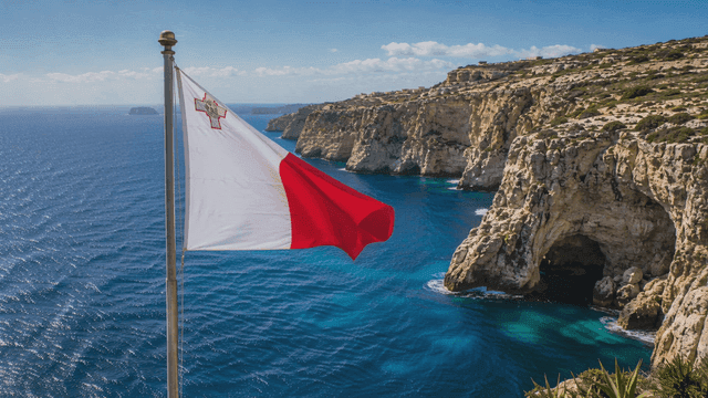 Maltese flag fluttering beside cliffs and sea