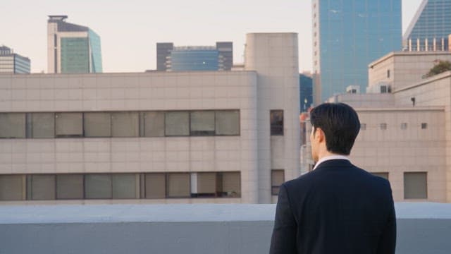 Man in a suit looking at buildings from a rooftop