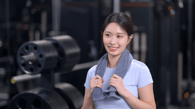 헬스장에서 수건을 두른 미소 짓는 젊은 여성의 옆모습