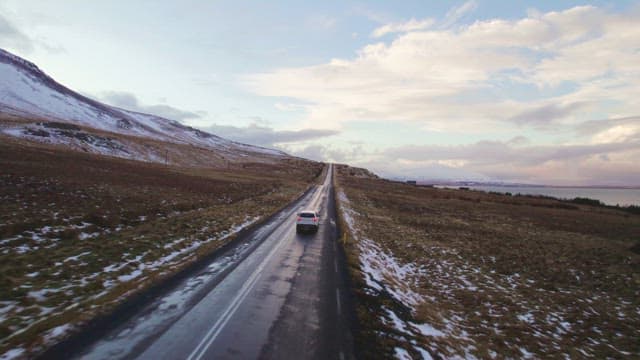 Car driving on the road next to a snowy mountain