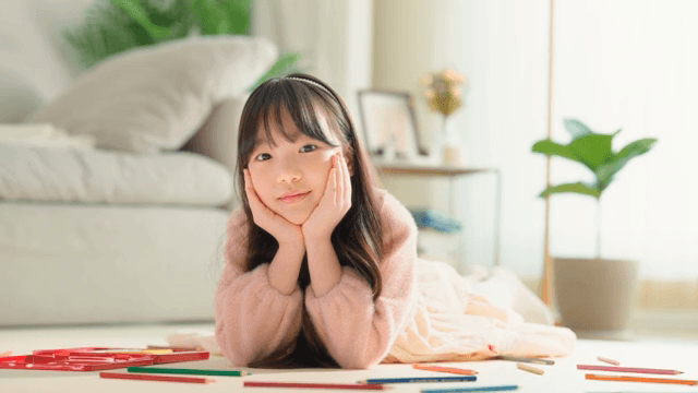 Child lying on the living room floor making a flower pose with their hands