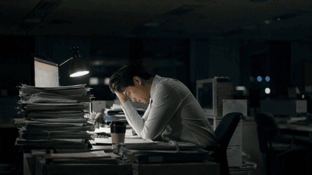 Office worker covering their head in office late at night