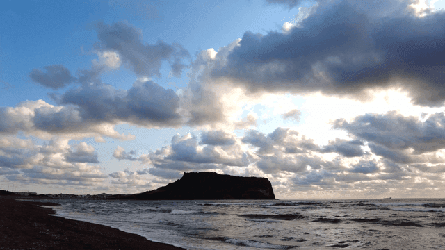Island with crashing waves beneath clouds early in morning