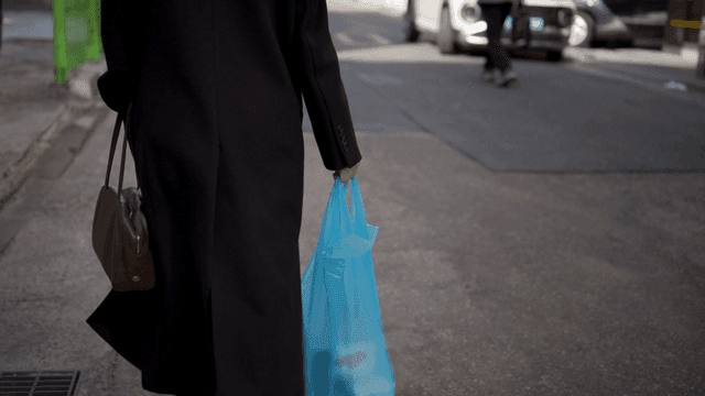 Woman walking down street carrying plastic bag