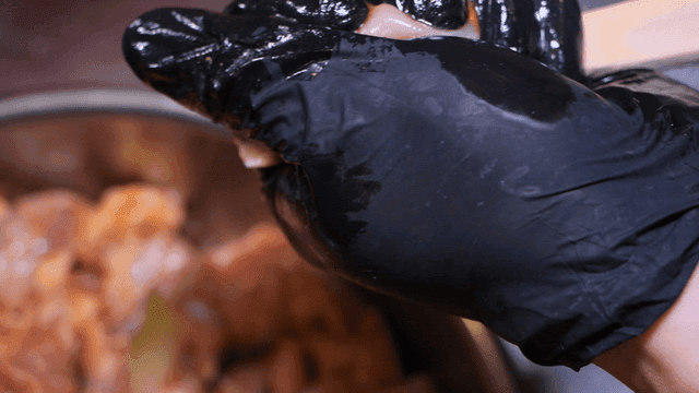 Gloved hands skewering raw meat pieces