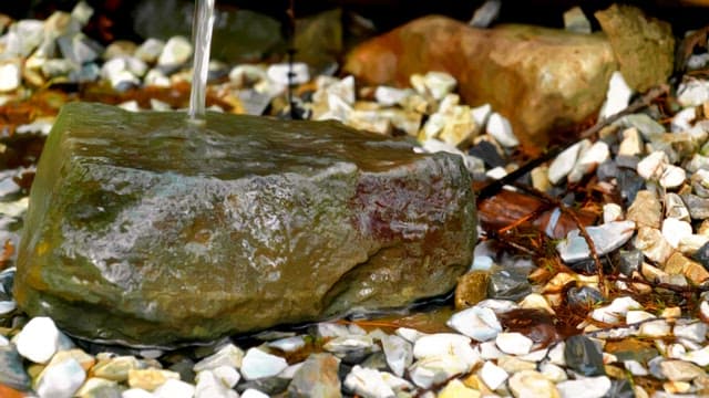 Water trickles over a mossy rock surrounded by pebbles