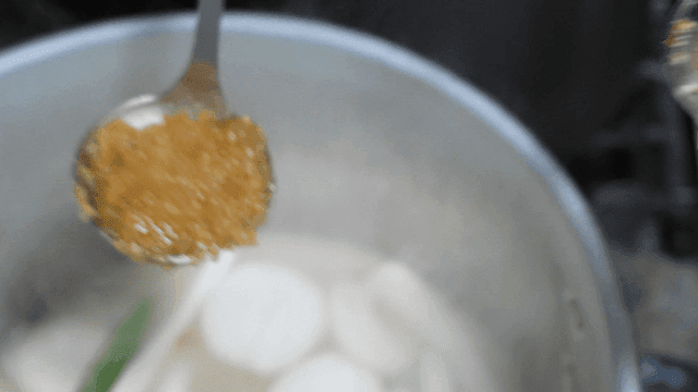 Ladleful of minced garlic in pot full of broth