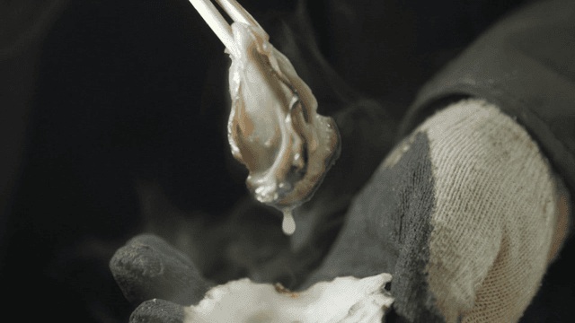 Freshly steamed oyster being held with chopsticks