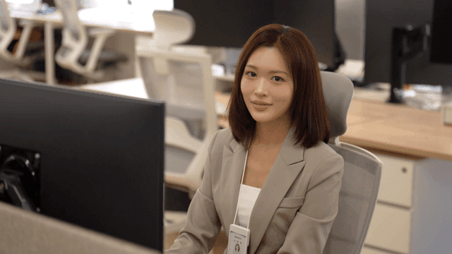Woman smiling while looking straight ahead while sitting at desk working in office
