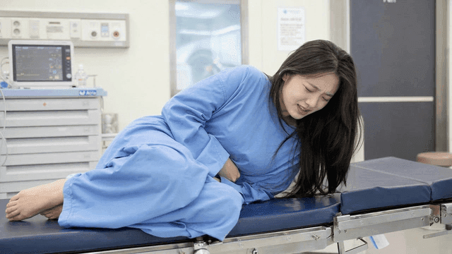 Female patient clutching her stomach in pain on hospital bed