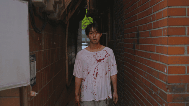 좁은 골목길을 걷는 피가 묻은 옷을 입은 망치를 든 남자