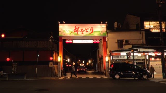 Night street scene with pedestrians and vehicles near a well-lit traditional gate