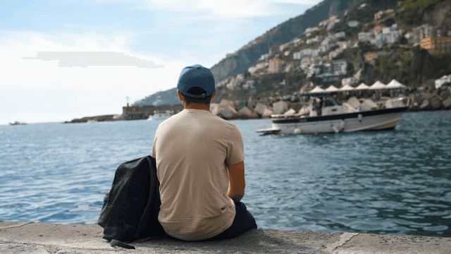 Man sitting by the sea with boats passing