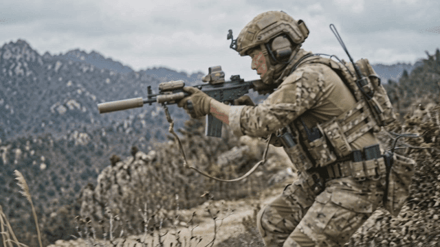 Soldier in camouflage moving through rugged terrain.
