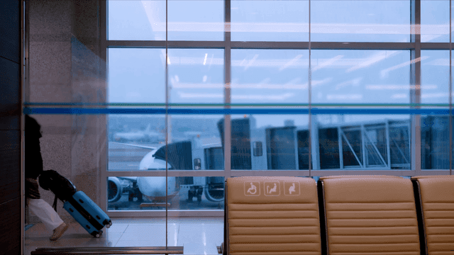 Passengers walking in airport terminal where airplanes are visible