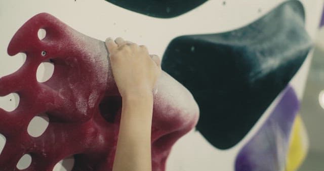 실내 클라이밍장에서 빨간색 홀드를 잡고 있는 손