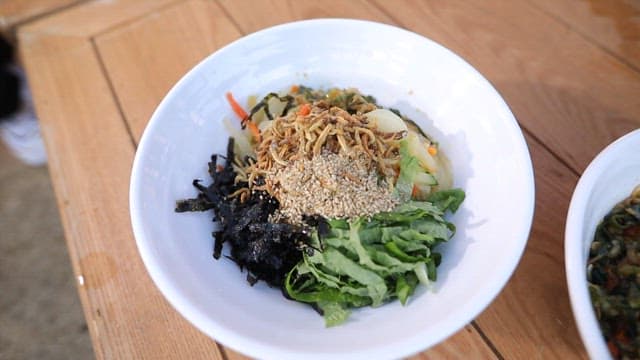 Two bowls of anchovy bibim noodle with vegetables and soy sauce